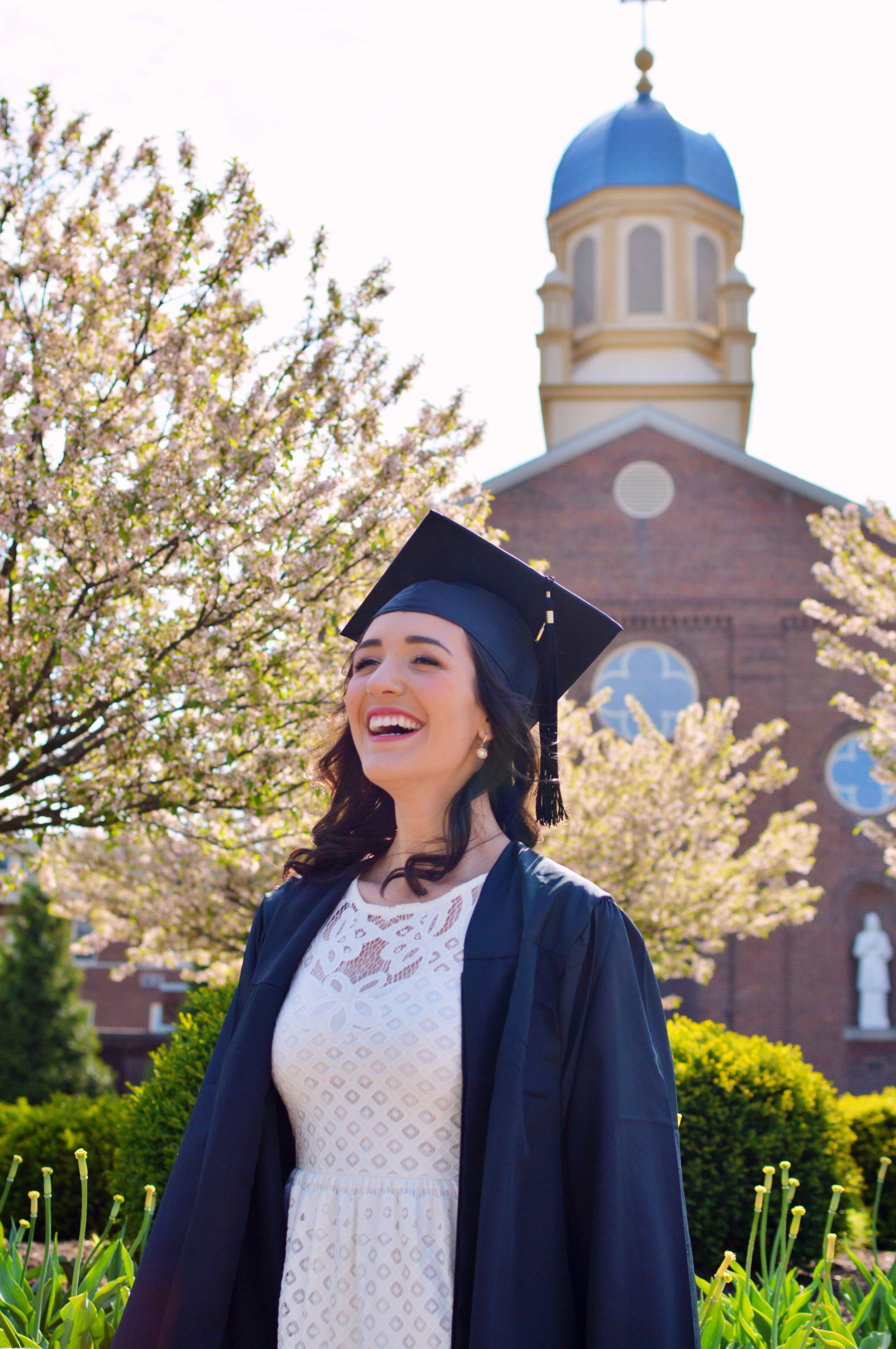 A graduate in cap and gown smiling outside her university on graduation day
